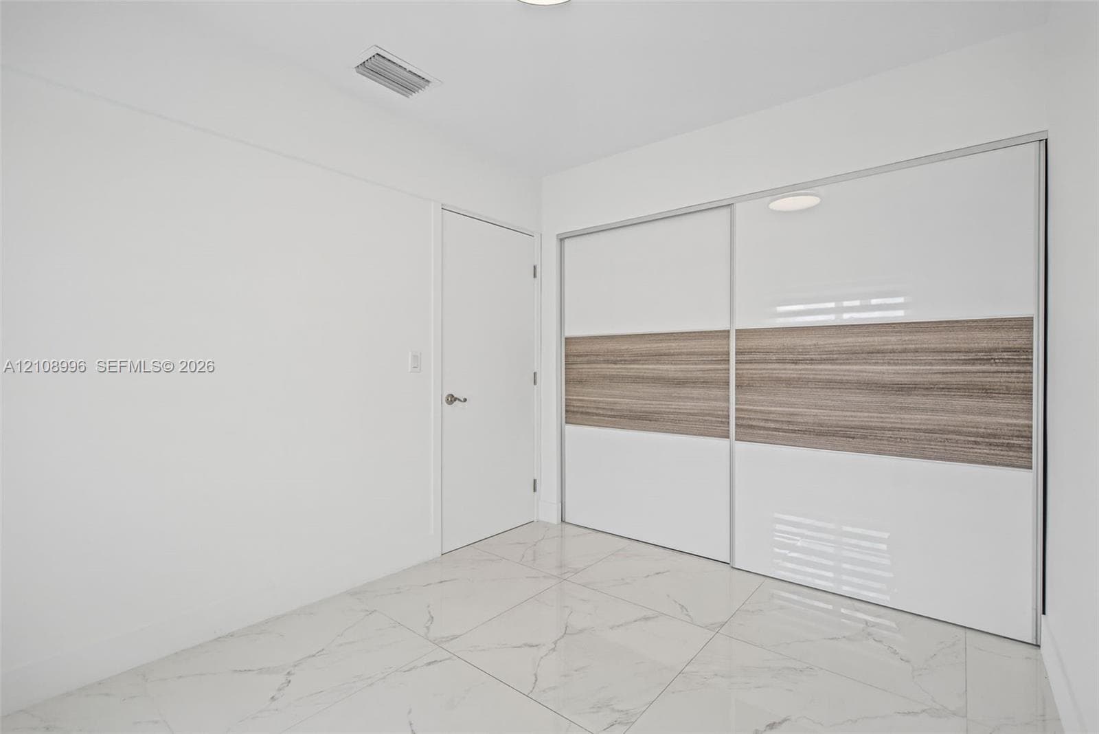 Large-format polished tile flooring featuring a veined pattern, dual sliding closet doors with high-gloss white and wood-finish detailing, and a solid-core interior door