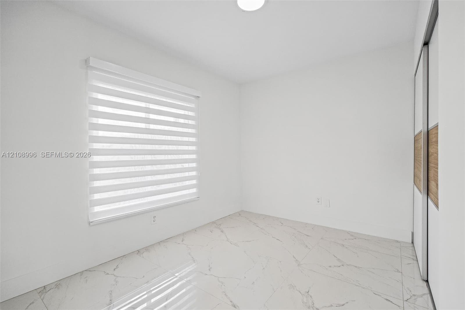 Large-format white tile flooring with veining, dual-panel sliding closet with wood-finish inlay, and adjustable window roller shades