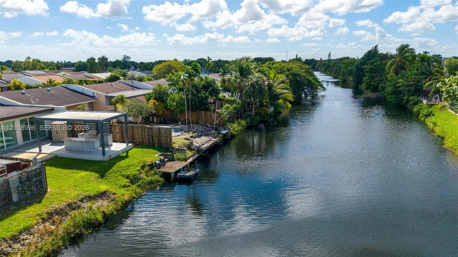 Waterfront property featuring a canal-side bulkhead, a private boat dock, and a covered outdoor kitchen structure situated on a grass-covered lot