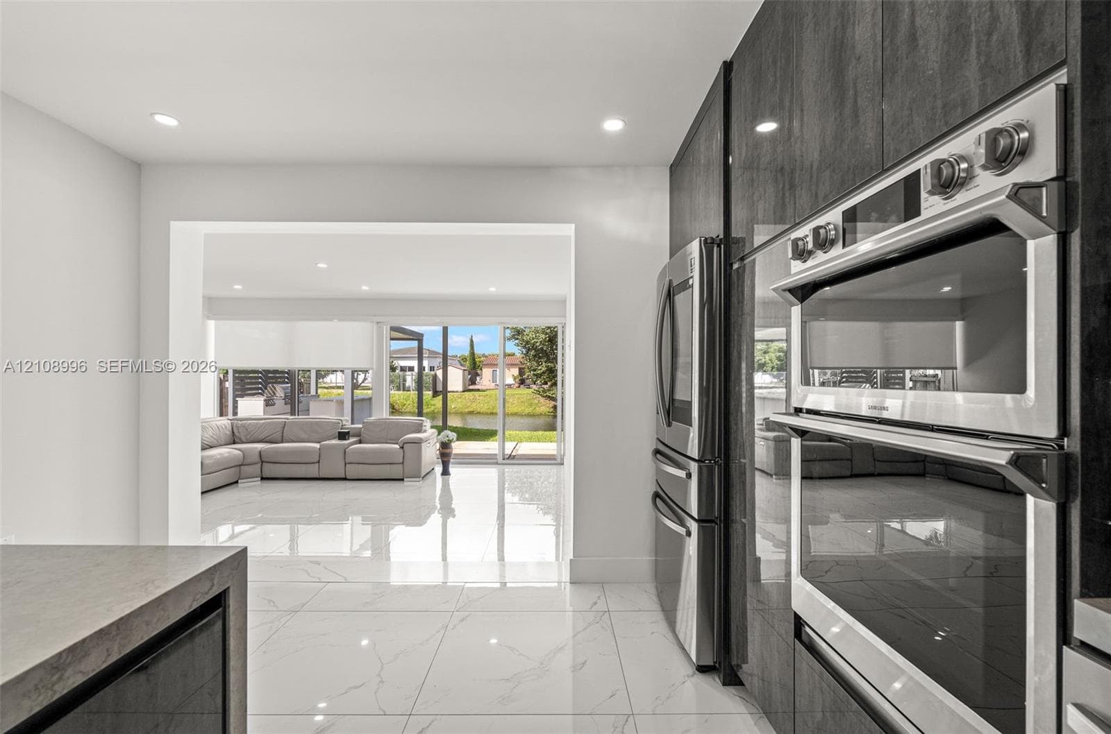 Modern kitchen featuring sleek, high-gloss charcoal cabinetry, integrated stainless steel double wall ovens, a stainless steel refrigerator, and large-format porcelain tile flooring