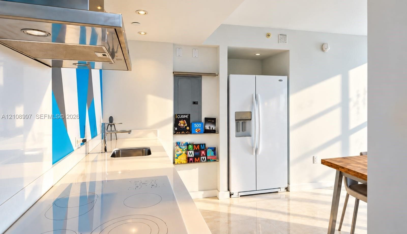 Kitchen featuring a smooth-top electric cooktop, stainless steel range hood, stone-surface countertop with integrated sink, and white side-by-side refrigerator