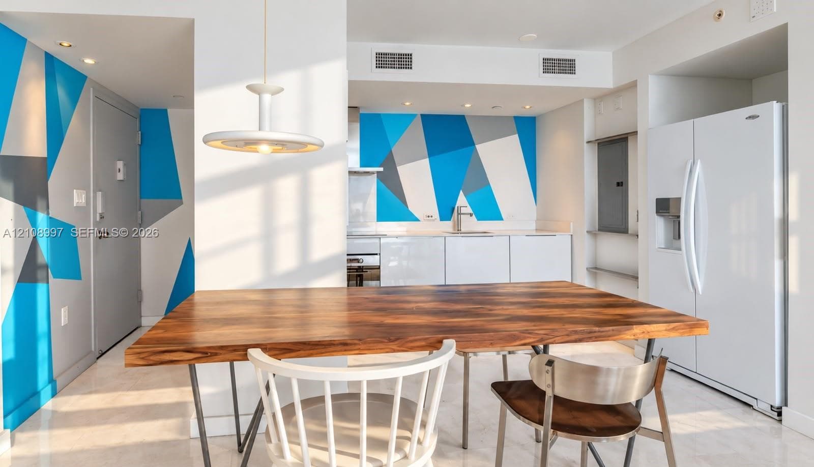 Kitchen featuring white cabinetry, geometric wall murals, sleek metal appliances, stone-finish flooring, and a modern pendant light fixture