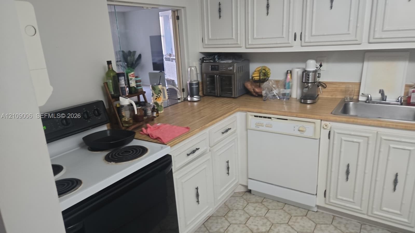 Kitchen featuring white raised-panel cabinetry, wood-finish countertops, stainless steel sink with chrome faucet, built-in dishwasher, and electric range