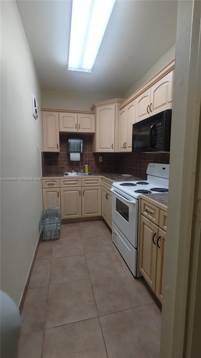 Kitchen featuring light-finish cabinetry, tile flooring, dark-toned tile backsplash, integrated microwave, and white freestanding range