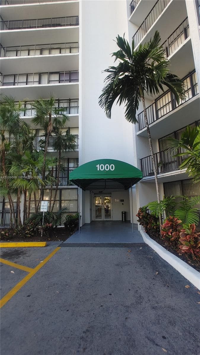 High-rise exterior featuring private balconies, a covered entrance with a green awning, and established tropical landscaping