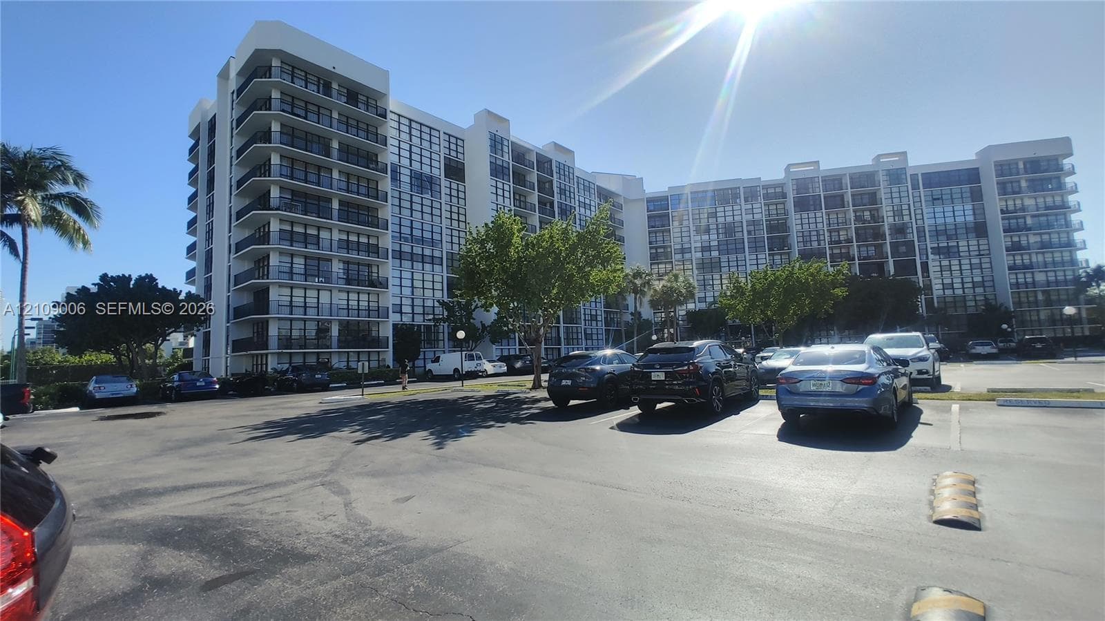 Mid-rise residential building exterior featuring a white facade, floor-to-ceiling windows, and private balconies, complemented by surface parking
