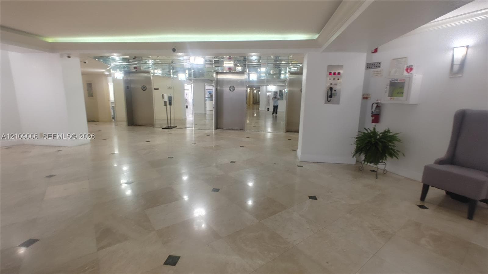Lobby featuring polished stone flooring with inlaid tile accents, stainless steel elevator doors, mirrored wall paneling, and recessed ceiling lighting