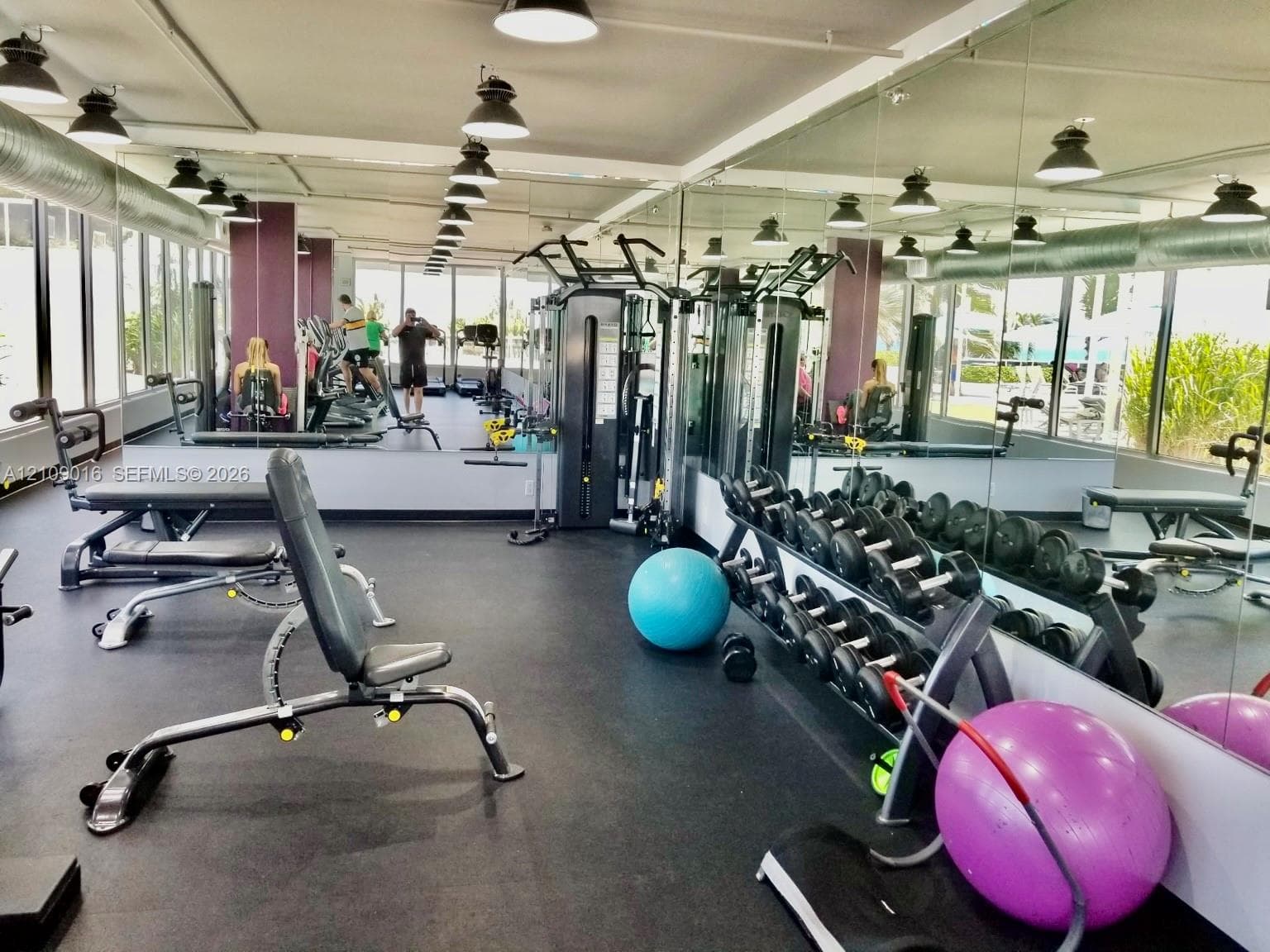 Fitness center featuring floor-to-ceiling mirror walls, expansive window lines, industrial-style exposed ductwork, rubber flooring, and overhead pendant lighting