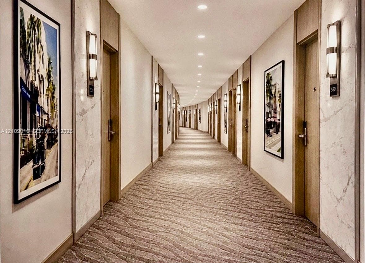 Hallway featuring stone-finish wall paneling, textured carpeted flooring, wall-mounted sconce lighting, recessed ceiling lights, and flat-panel doors