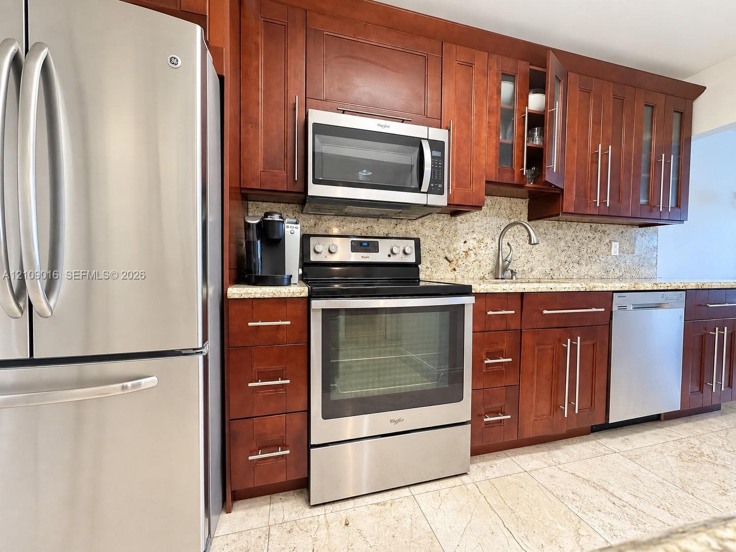 Kitchen featuring stained wood cabinetry, stone countertops, stainless steel appliances, and tile flooring