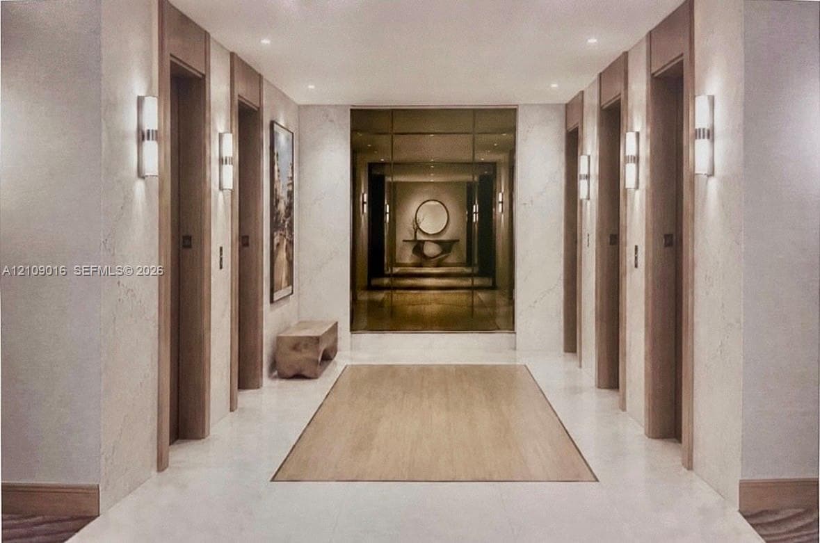 Foyer featuring large-format stone flooring, wood-paneled elevator surrounds, vertical wall sconces, and a full-height mirrored accent wall