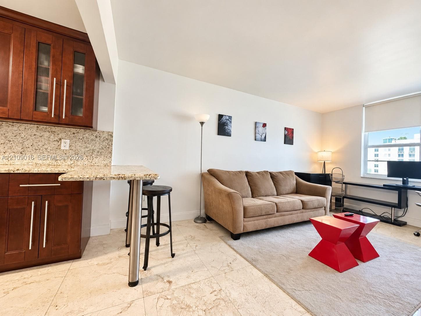 Kitchen area featuring cherry-finish cabinetry with glass-paneled upper doors, stone-composite countertops, and a breakfast bar with a brushed metal support pillar, complemented by large-format tile flooring throughout