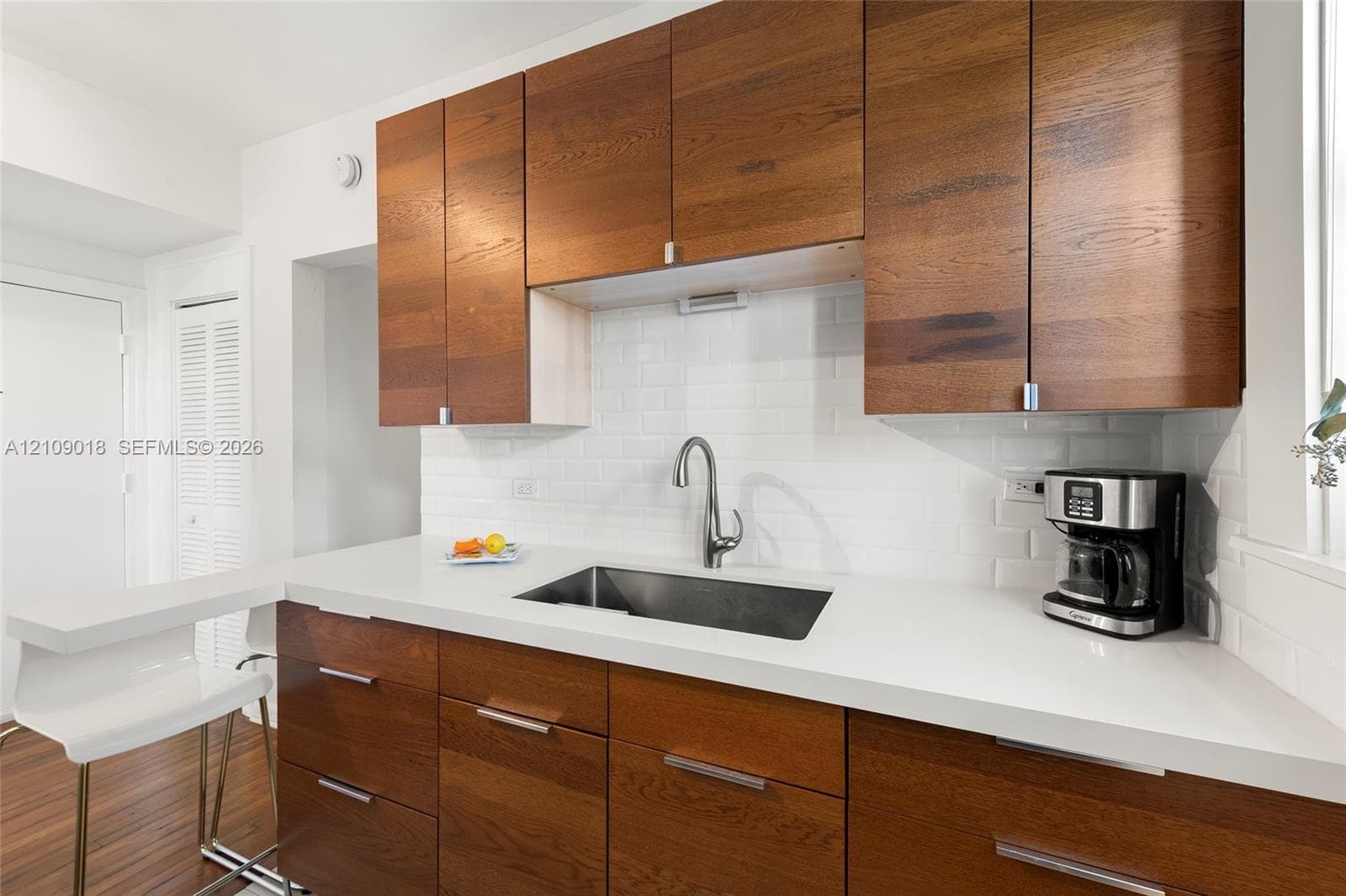 Kitchen featuring natural wood-finish cabinetry, solid surface countertops, white subway tile backsplash, stainless steel undermount sink, and a gooseneck faucet
