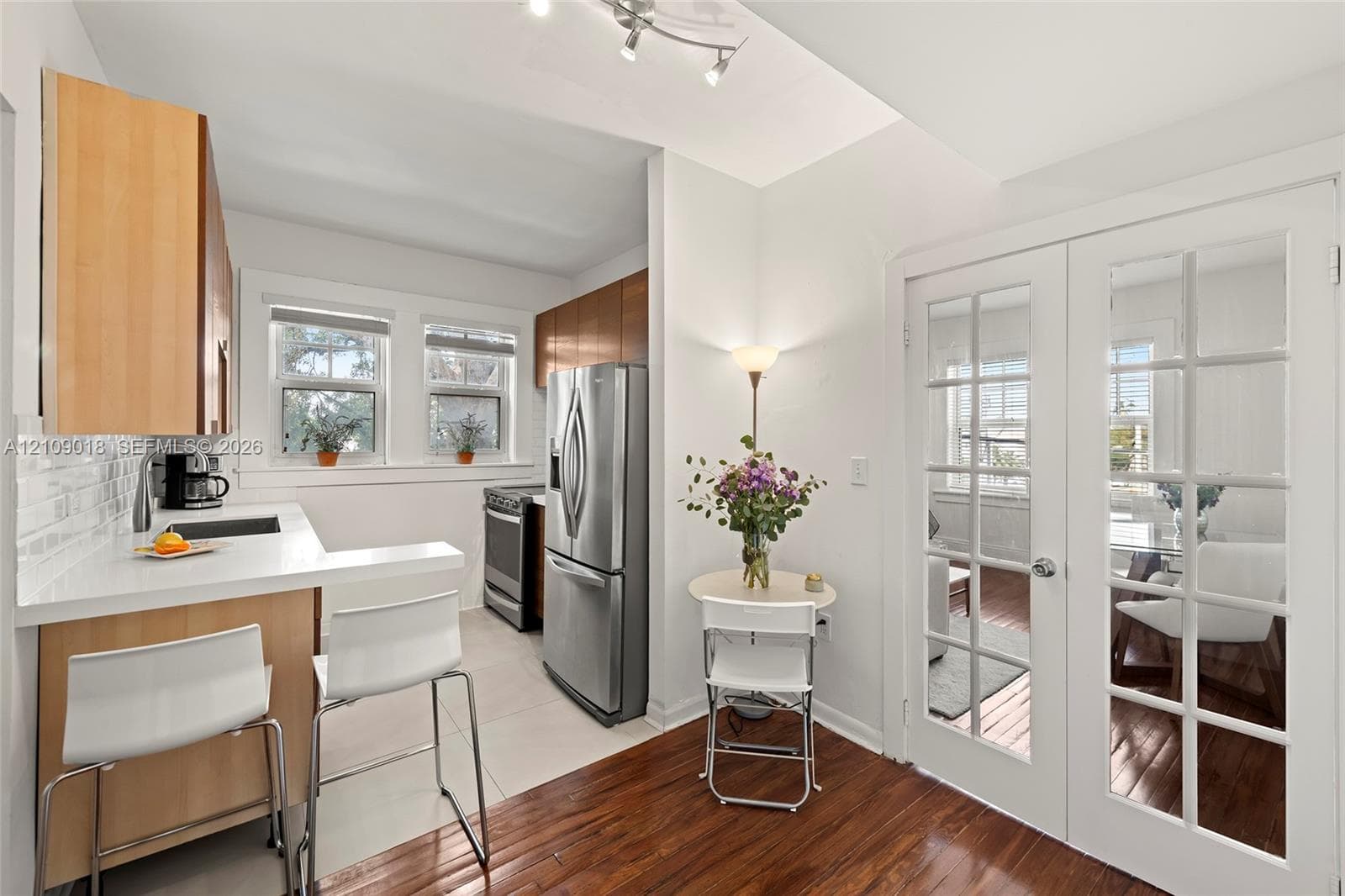 Kitchen featuring light wood-finish cabinetry, solid-surface countertops, subway tile backsplash, stainless steel appliances, and French doors with glass panes