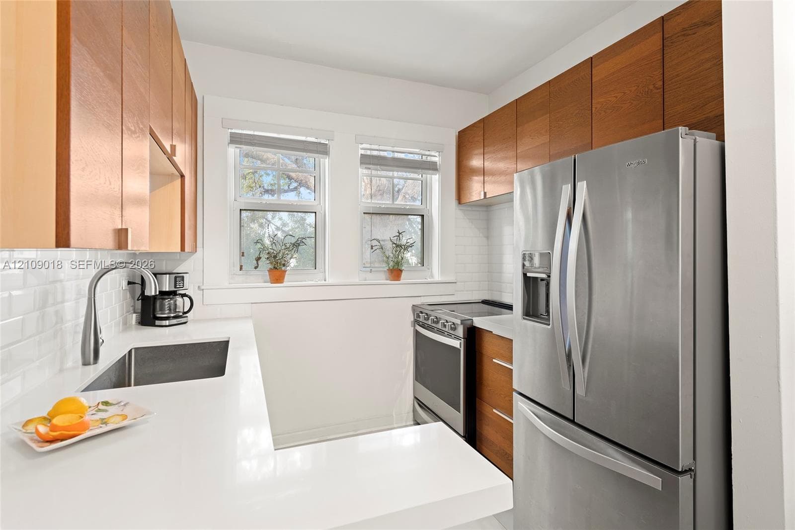 Kitchen featuring wood-finish cabinetry, white solid-surface countertops, subway tile backsplash, stainless steel appliances, and a stainless steel undermount sink with a gooseneck faucet