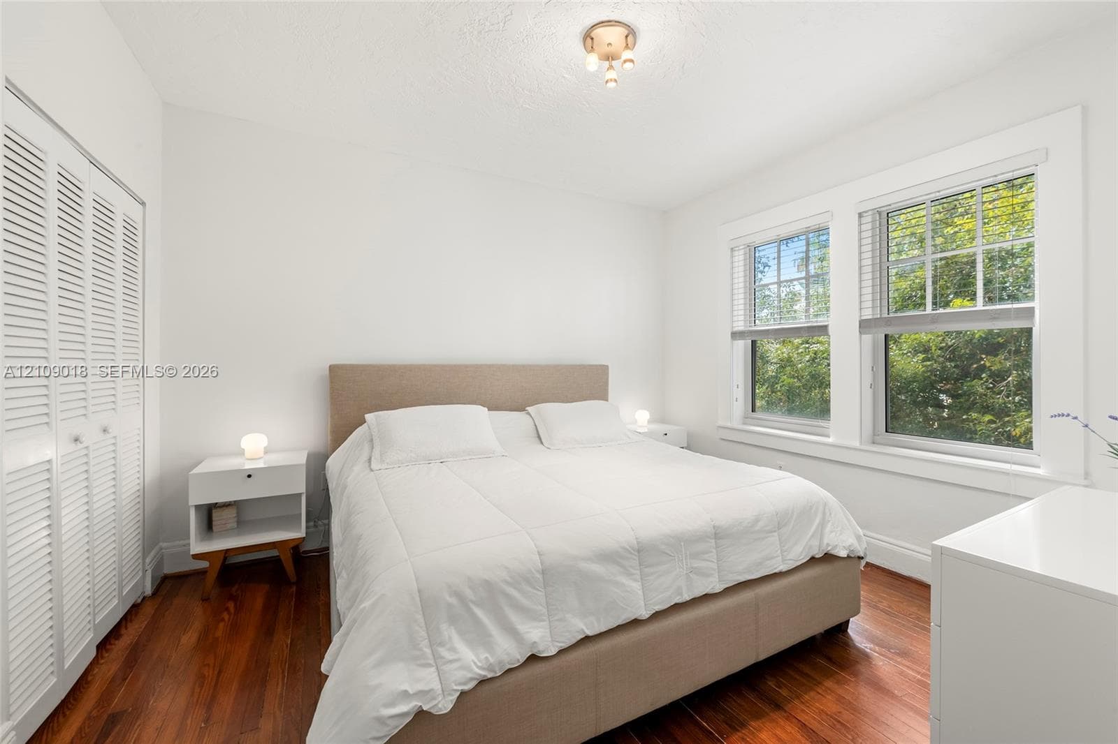 Room with wood-finish flooring, dual windows with grid-patterned glass, and white louvered closet doors