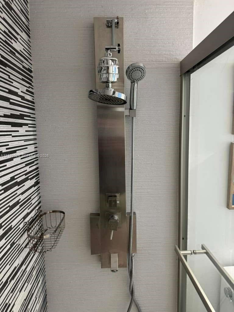 Brushed stainless steel shower panel system featuring an integrated rainfall showerhead, adjustable handheld shower wand, and single-handle mixing valve, set against textured wall tile
