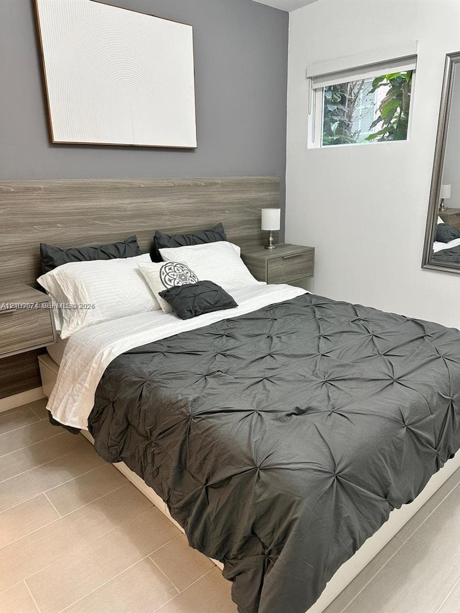 Built-in wood-finish headboard with integrated floating nightstands, neutral tile flooring, and a horizontal window with a fitted roller shade