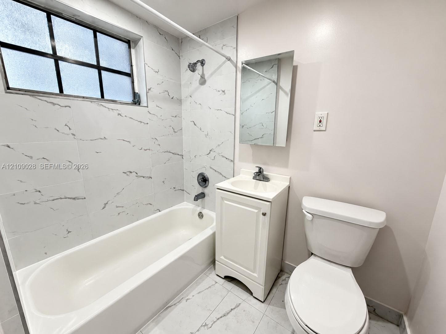 Bathroom featuring a tub with stone-patterned tile surround, grid-pane window, pedestal vanity with sink, and floor-to-ceiling stone-patterned tile flooring