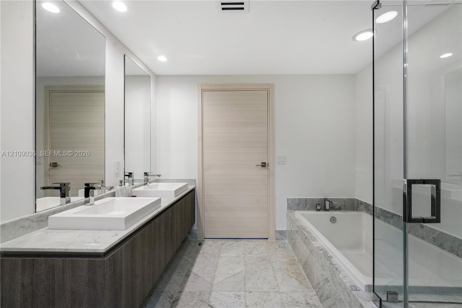 Floating double vanity with dual rectangular vessel sinks, stone-surface countertop, floor-to-ceiling mirrors, recessed lighting, and a glass-enclosed shower with a deep soaking tub