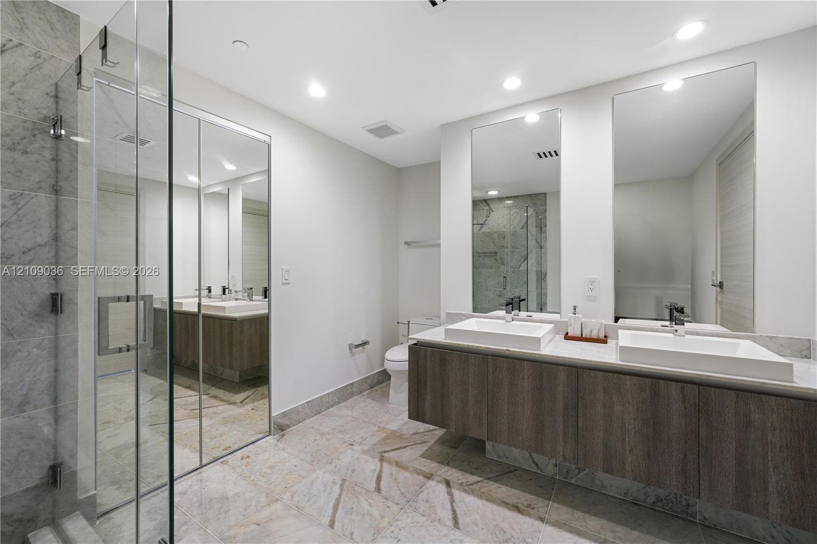 Floating double vanity with rectangular vessel sinks, floor-to-ceiling tiled glass-enclosed shower, stone-finish flooring, and dual wall-mounted mirrors