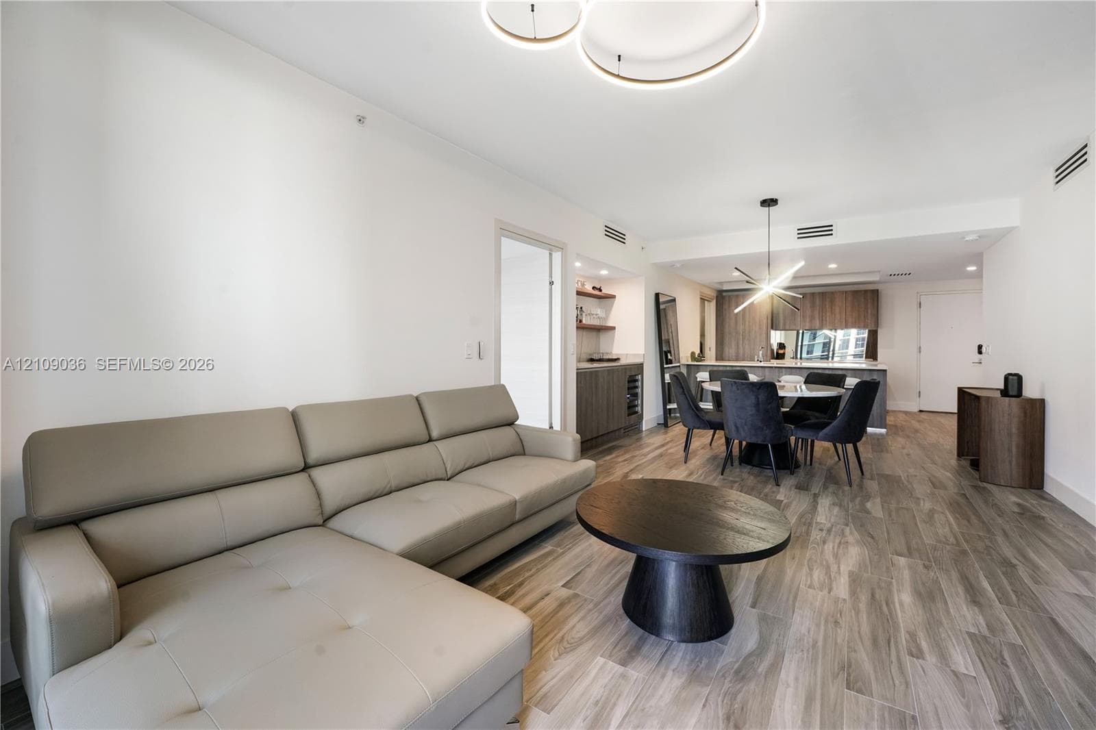 Open floor plan featuring wood-finish flooring, recessed lighting, modern circular halo chandelier, built-in wet bar with cabinetry, and kitchen with a central island