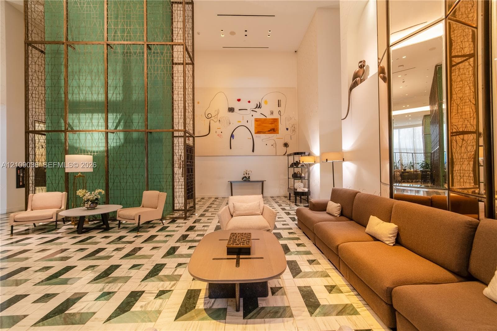 Grand lobby featuring expansive ceiling heights, geometric stone flooring, floor-to-ceiling decorative metal screening, mirrored wall panels, and recessed ceiling lighting