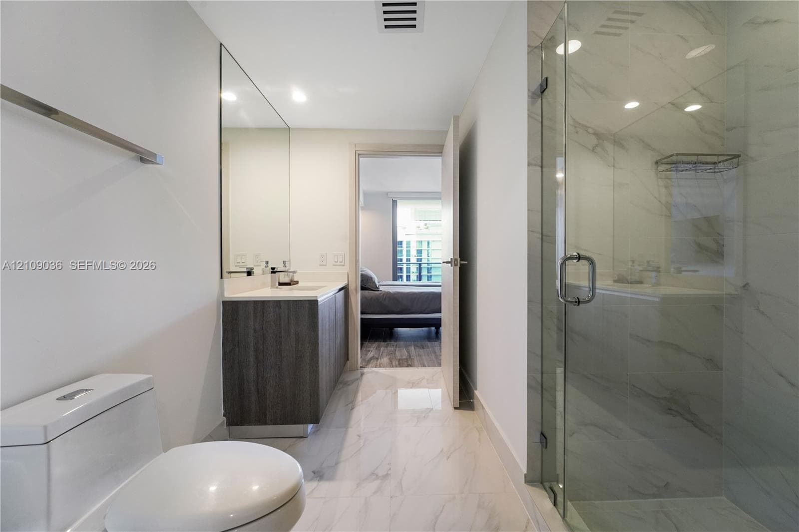 Bathroom featuring a dark wood-finish vanity, light-toned stone-style tile flooring, floor-to-ceiling vanity mirror, and a glass-enclosed shower with full-height stone-style wall tile