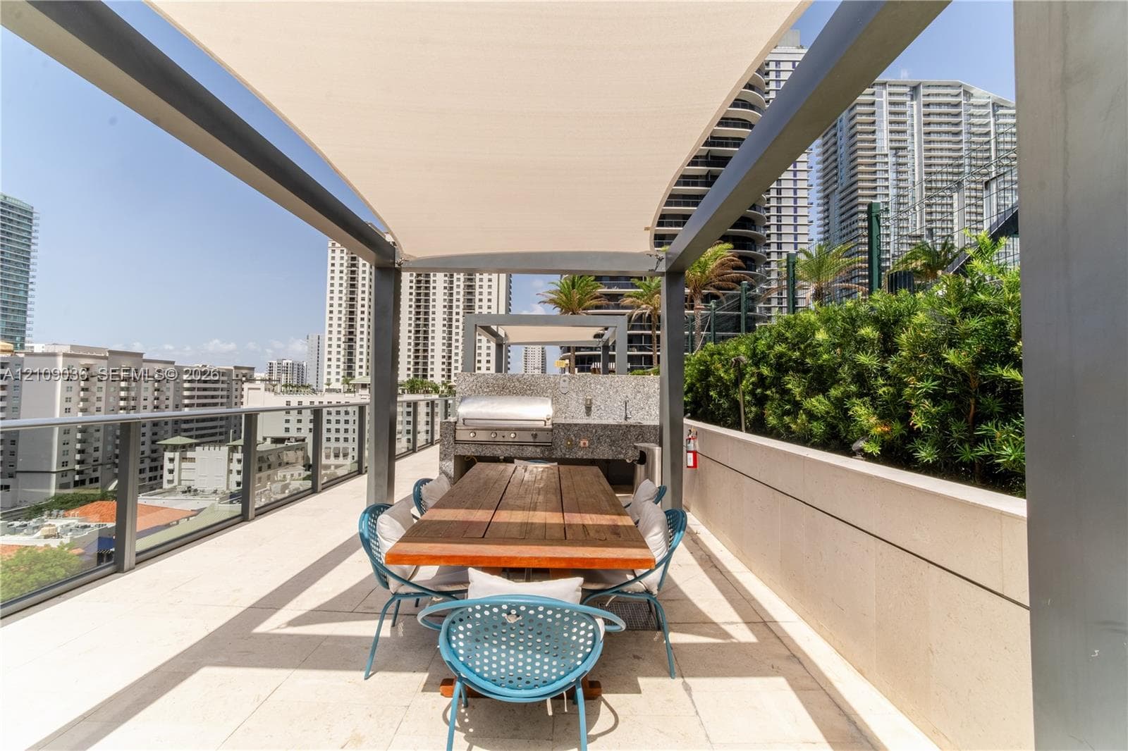 Rooftop terrace featuring a stone-topped outdoor kitchen, integrated gas grill, tension fabric shade structure, glass balcony railing, and stone tile flooring