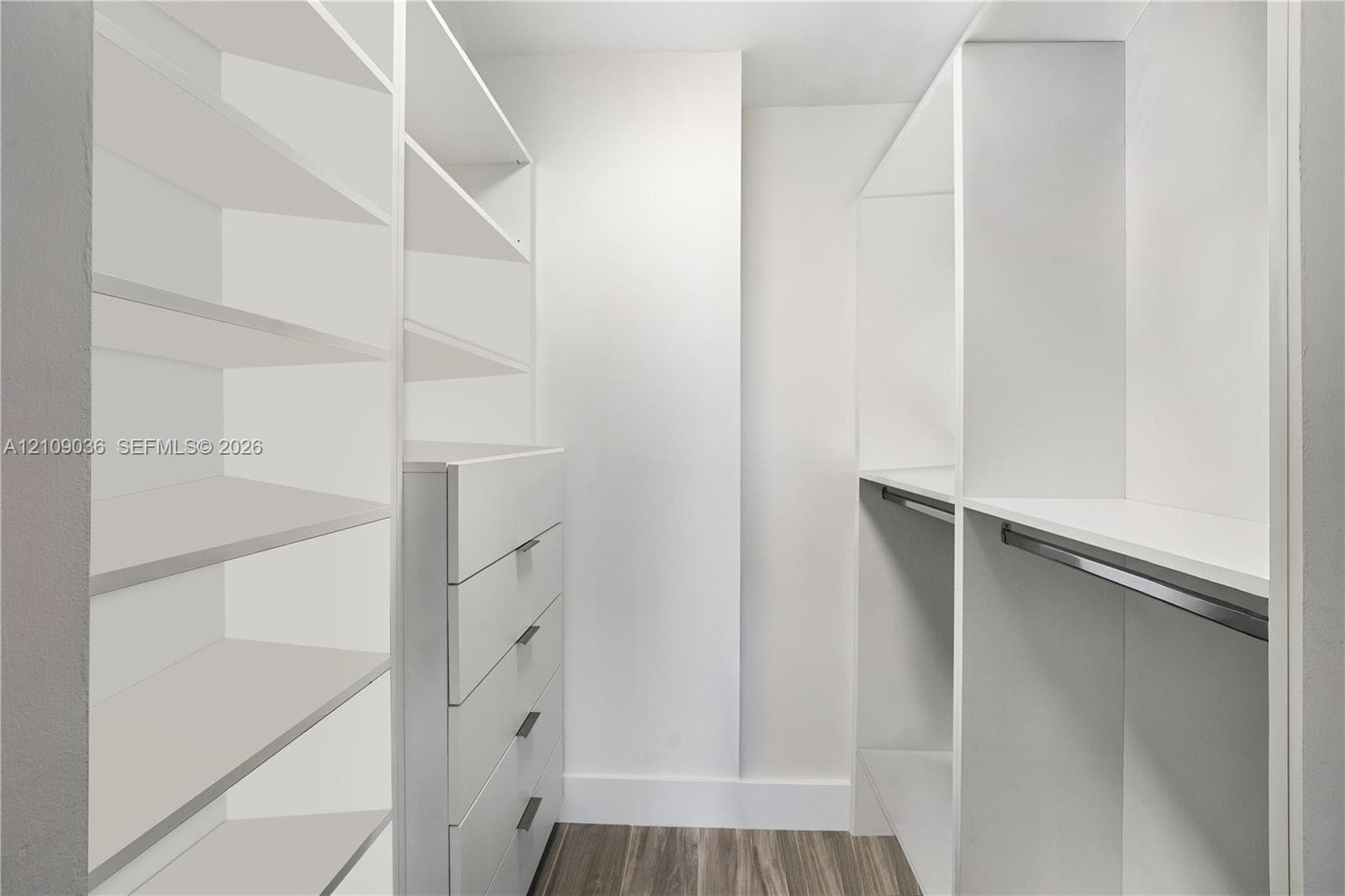 Walk-in closet featuring white built-in shelving, integrated dresser drawers with bar pulls, and a metal hanging rod over wood-finish flooring