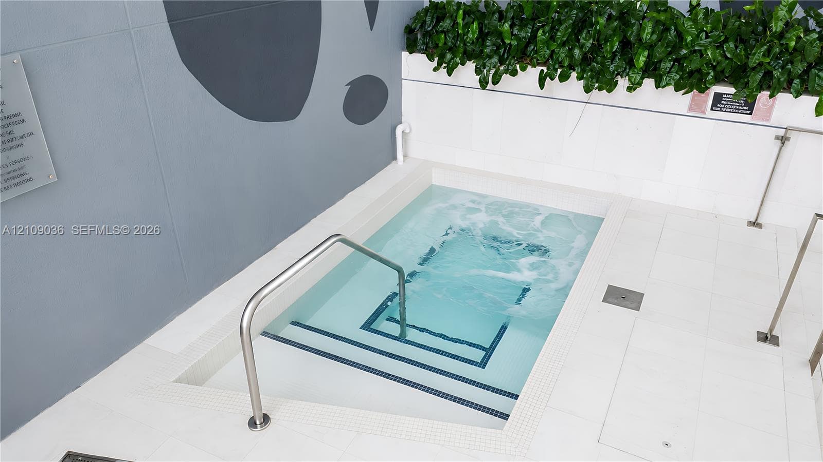 In-ground spa featuring white tile surround, stainless steel handrails, integrated tile steps, and masonry accent walls