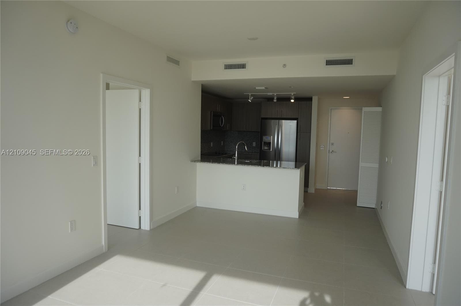 Open-concept kitchen featuring dark flat-panel cabinetry, stone countertops, stainless steel appliances, a gooseneck faucet, and large-format tile flooring