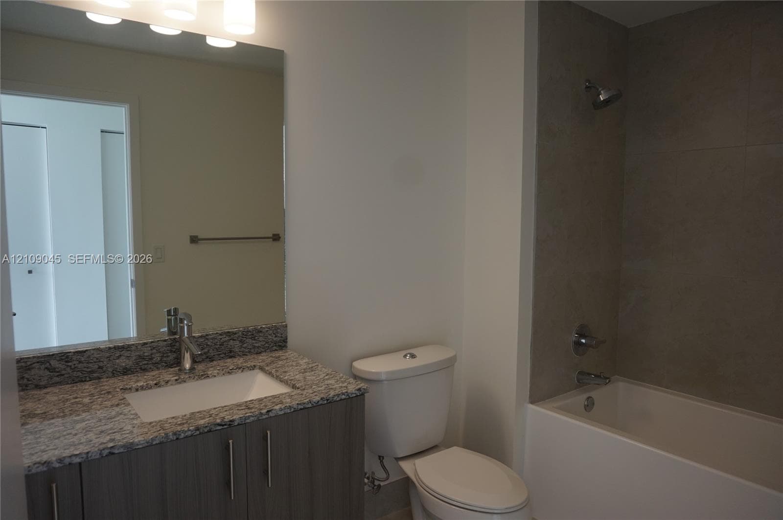 Bathroom featuring a stone-top vanity with an undermount sink, large wall-mounted mirror, brushed-nickel hardware, and a tub with a floor-to-ceiling tile surround