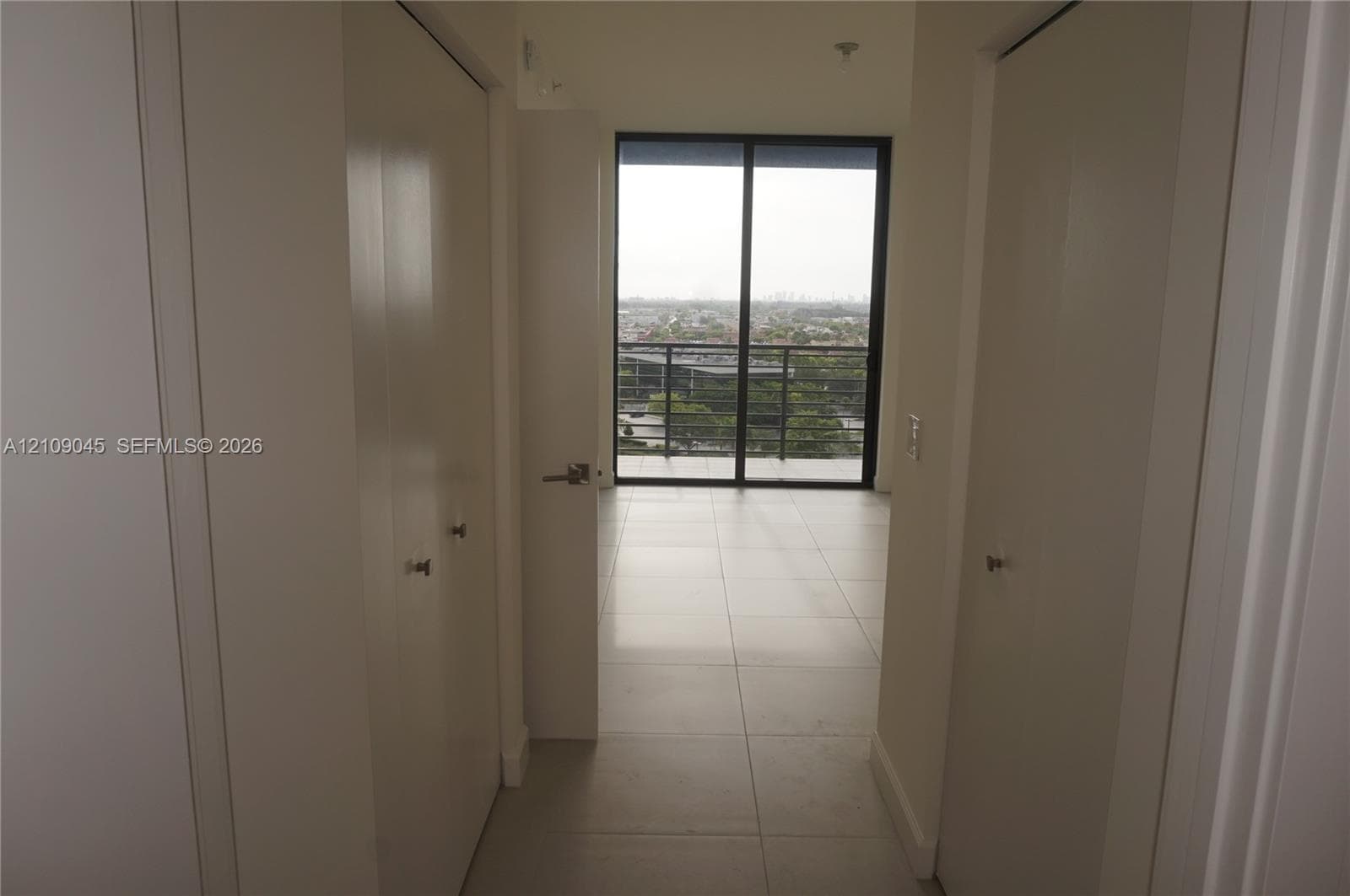 Neutral-toned tile flooring, dual closets with solid-panel doors, and floor-to-ceiling glass sliding doors opening to an exterior balcony