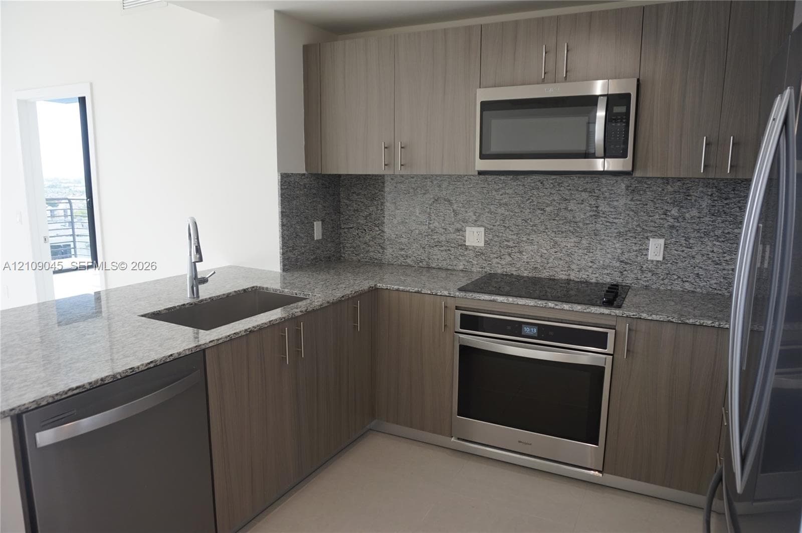 Kitchen featuring flat-panel wood-finish cabinetry, speckled stone countertops, a full-height stone backsplash, and stainless steel appliances including a built-in oven, microwave, and dishwasher