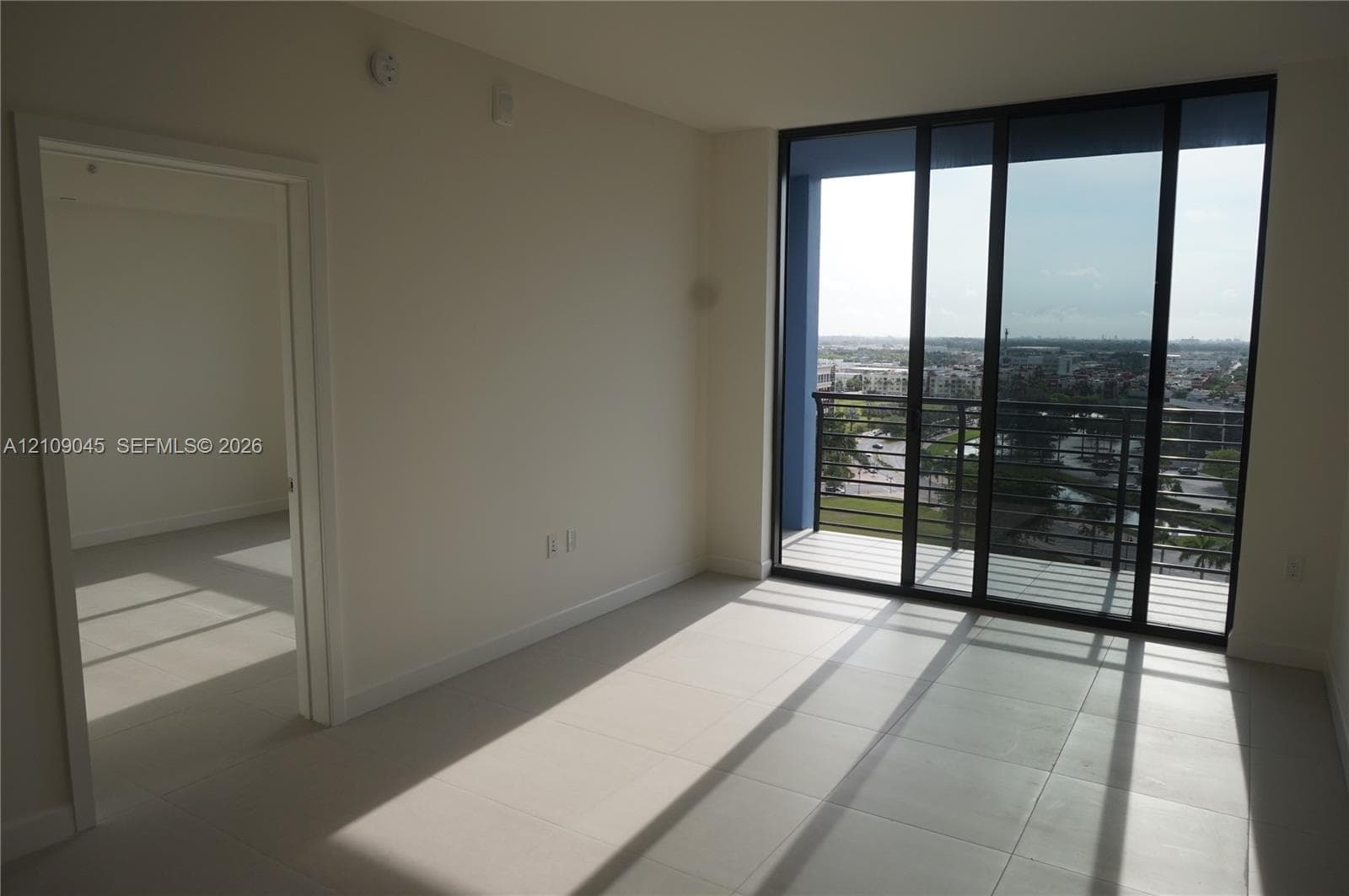 Large-format tile flooring, floor-to-ceiling glass sliding doors, and a private balcony with metal railings
