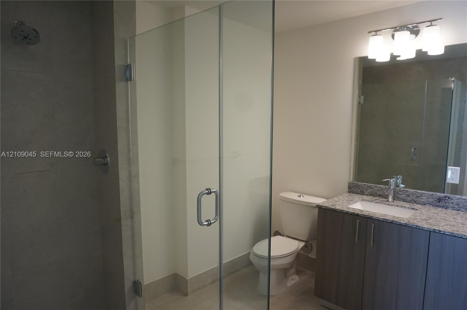 Bathroom featuring a walk-in shower with a frameless glass enclosure, vanity with stone-patterned countertop, under-mount sink, and multi-bulb integrated lighting