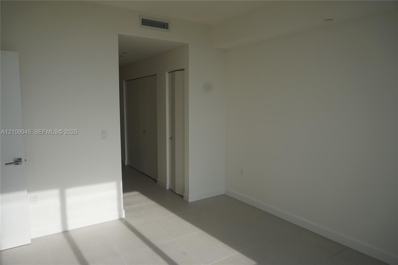 Neutral interior space featuring large-format ceramic floor tiles, recessed ceiling lighting, and multiple reach-in closets with doors