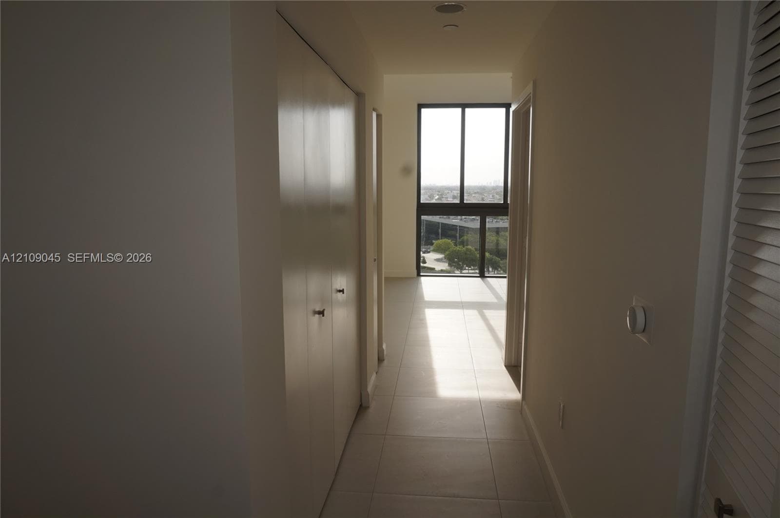 Hallway featuring large-format floor tile, double-door closet, and floor-to-ceiling windows