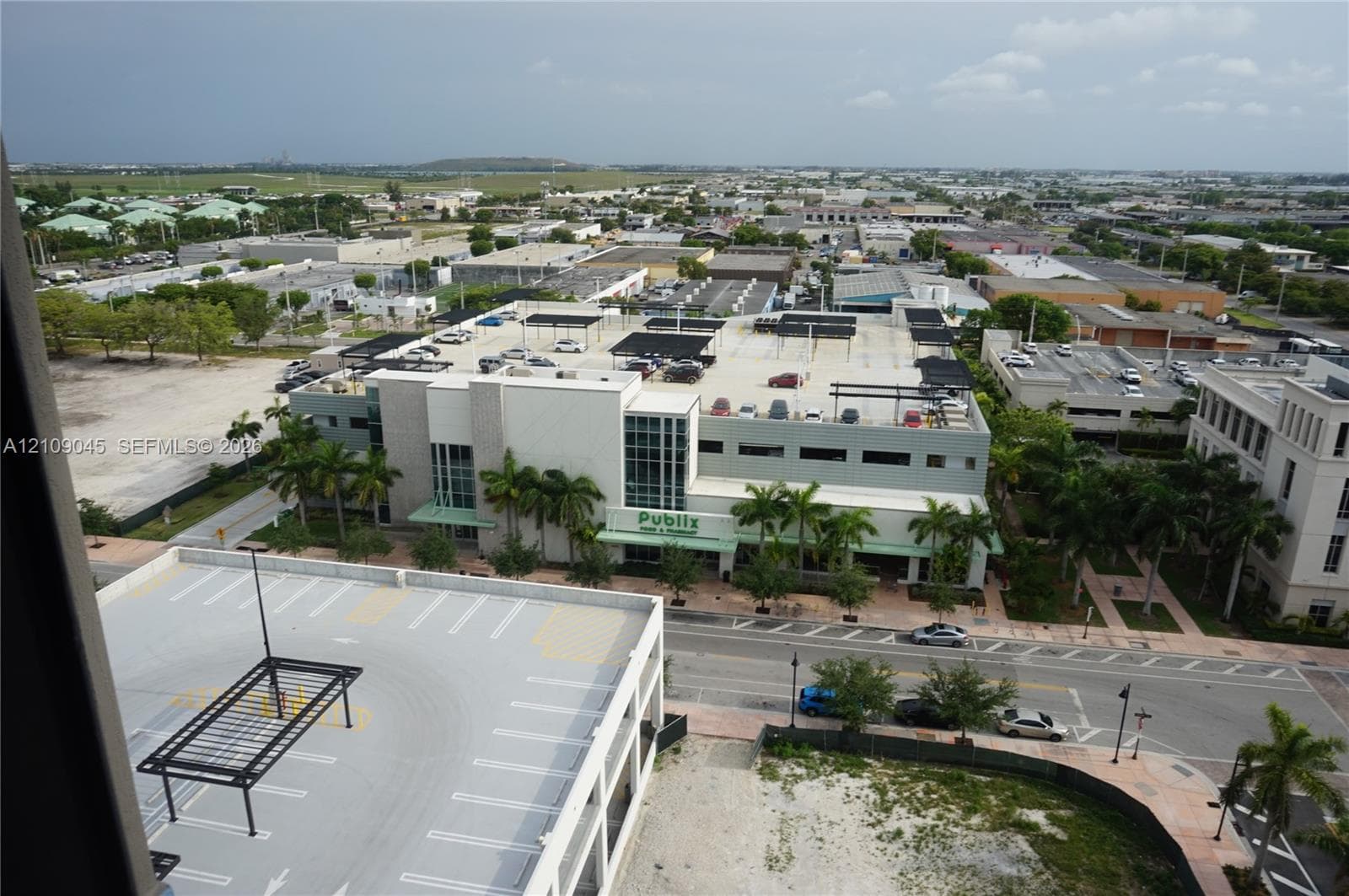 Aerial perspective featuring a multi-level parking structure with shaded upper-level canopy units, mature palm trees, and paved street access within a developed commercial area