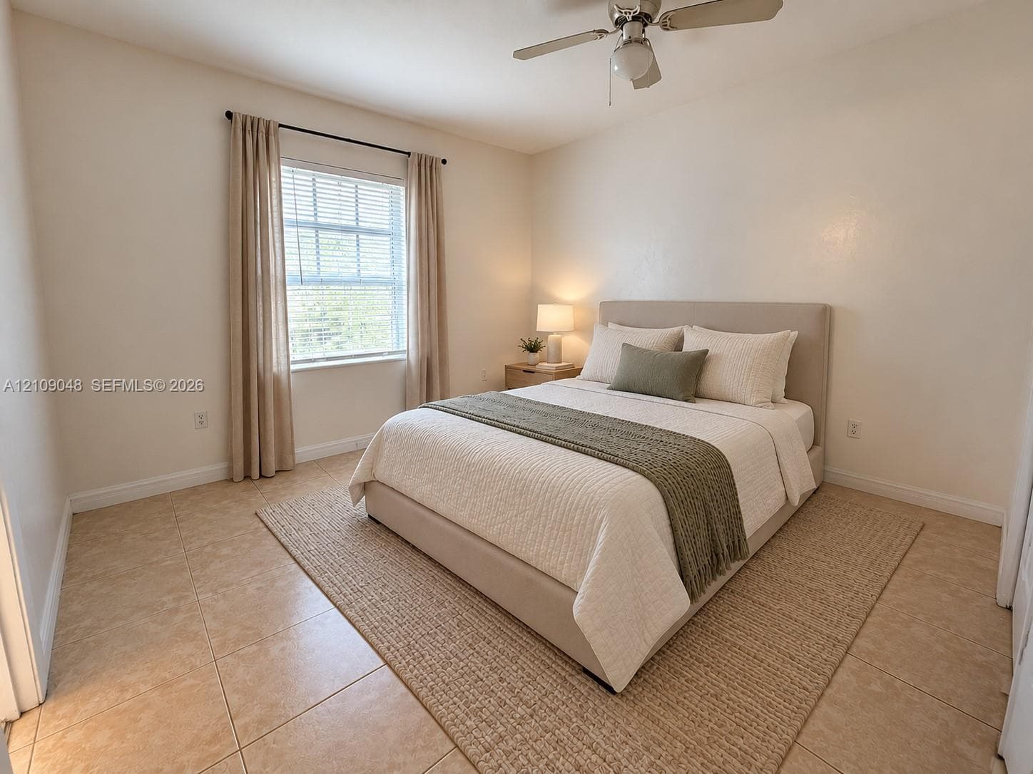 Neutral-toned room featuring large-format ceramic floor tiles, a dual-pane window, and a ceiling fan with integrated light fixture