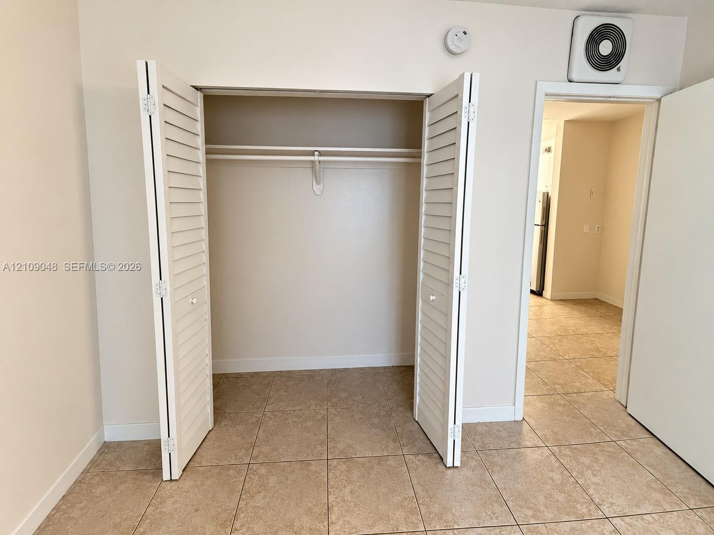 Closet featuring white louvered bifold doors and built-in shelving with an integrated rod, set against neutral wall finishes and ceramic tile flooring