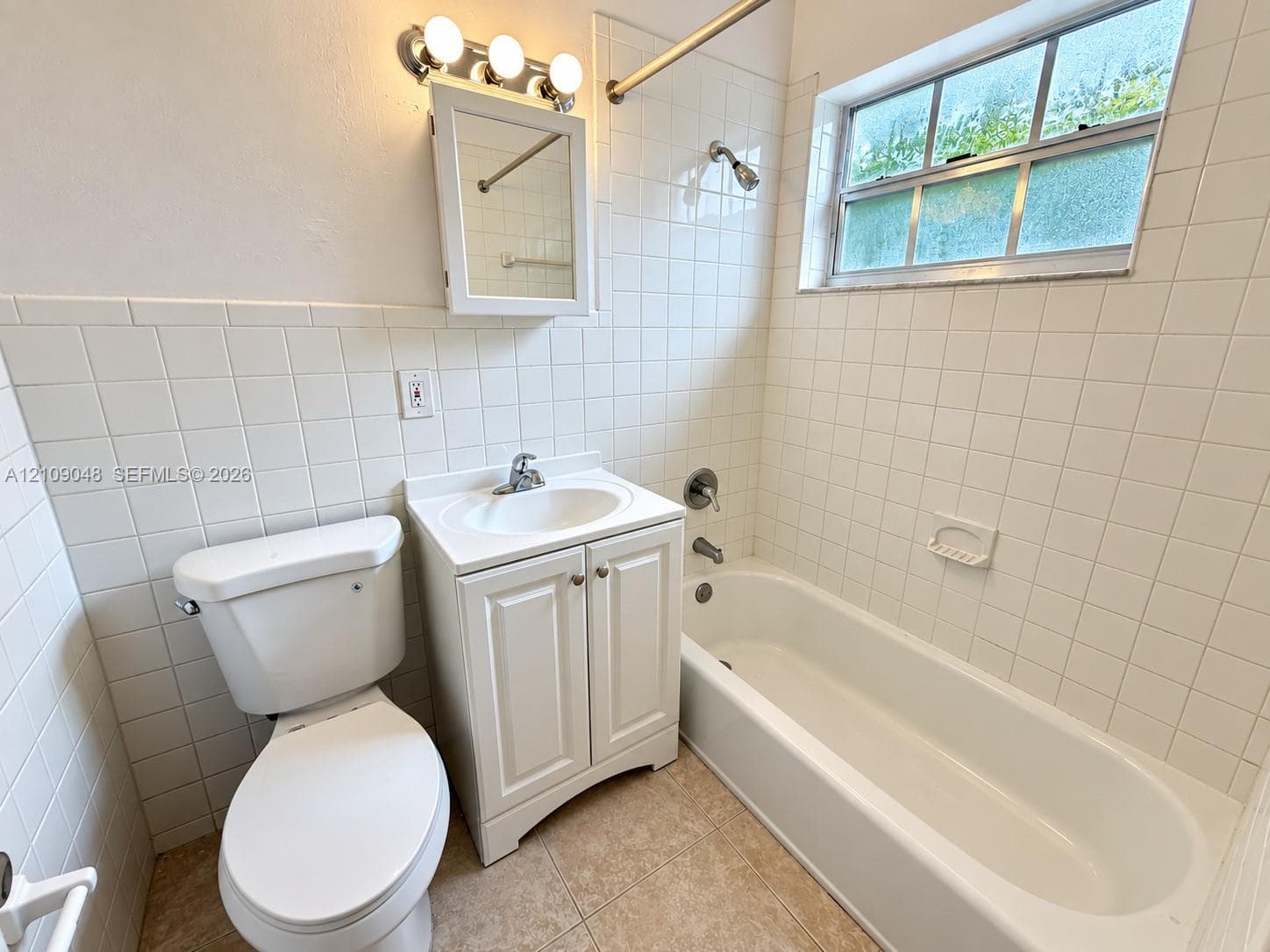 Bathroom featuring a porcelain tub-and-shower combination, white cabinetry vanity with a drop-in sink, wall-mounted medicine cabinet, and ceramic tile wall surround