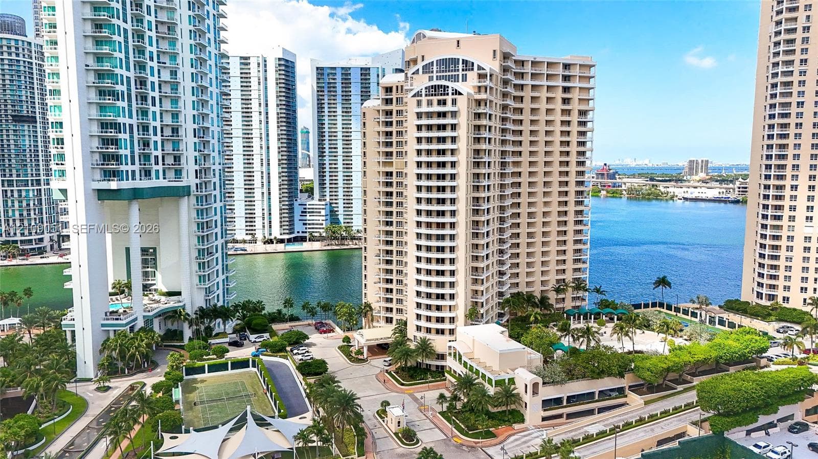 High-rise residential exterior featuring private balconies, tennis courts, a swimming pool, and gated entry, situated along the waterfront