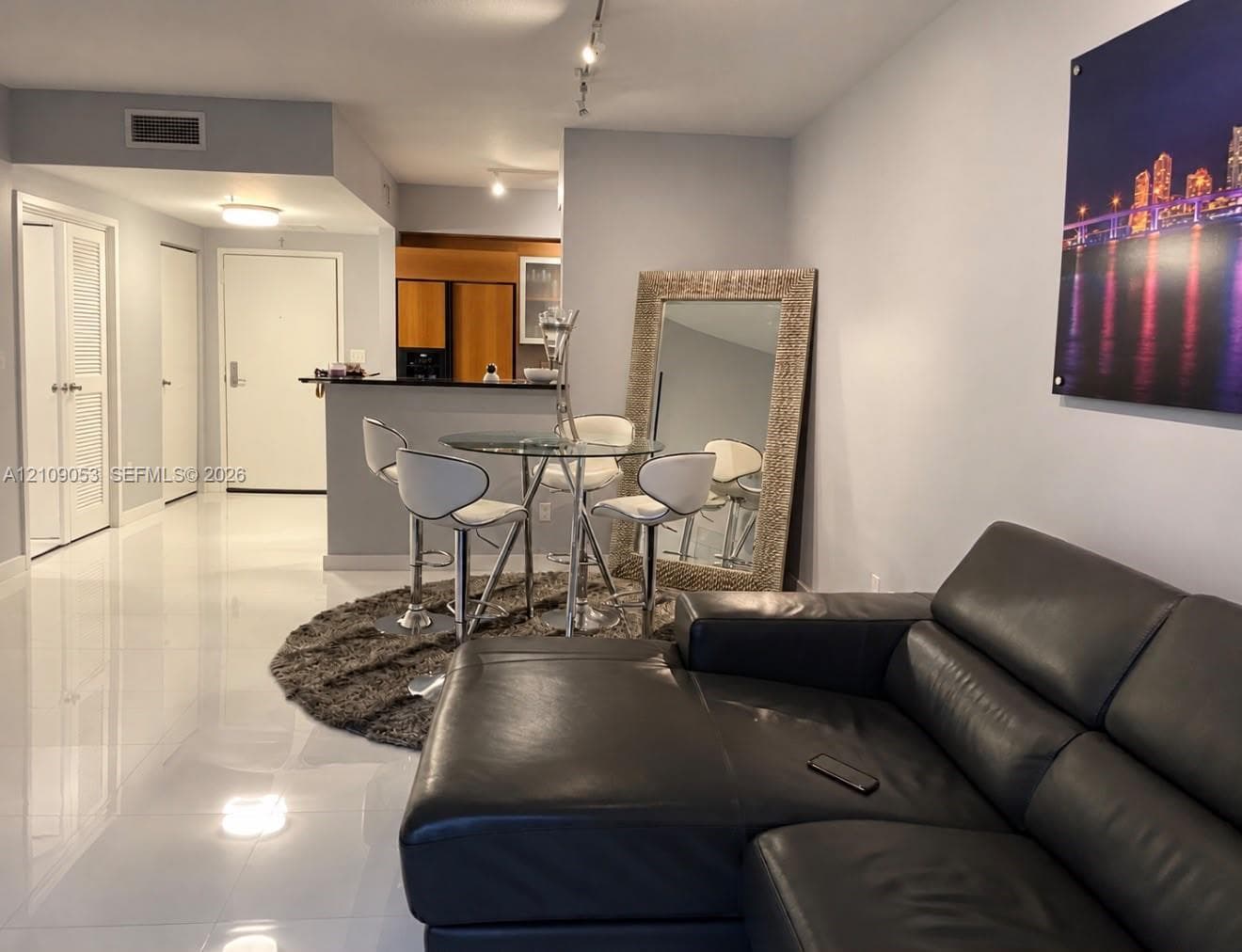 Open-concept interior featuring large-format white tile flooring, breakfast bar with a stone countertop, and adjustable track lighting