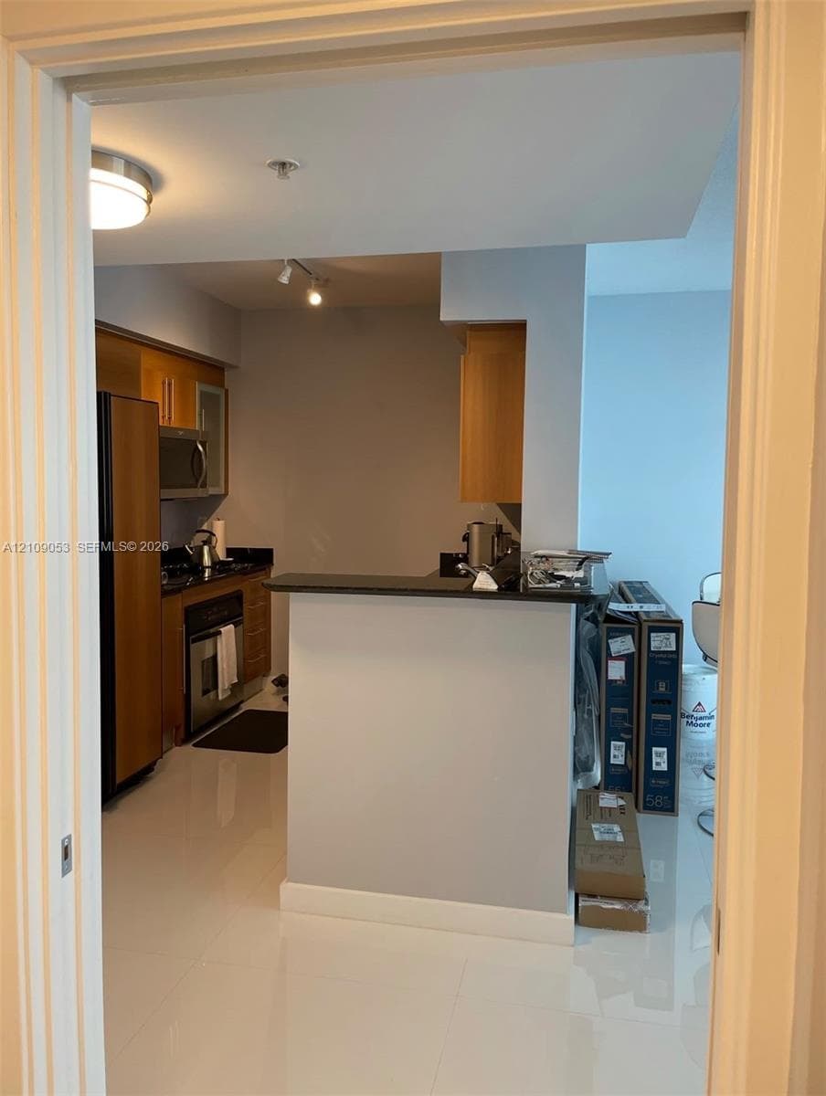 Kitchen featuring wood-finish cabinetry, stone countertops, stainless steel appliances, and tile flooring, complete with a breakfast bar