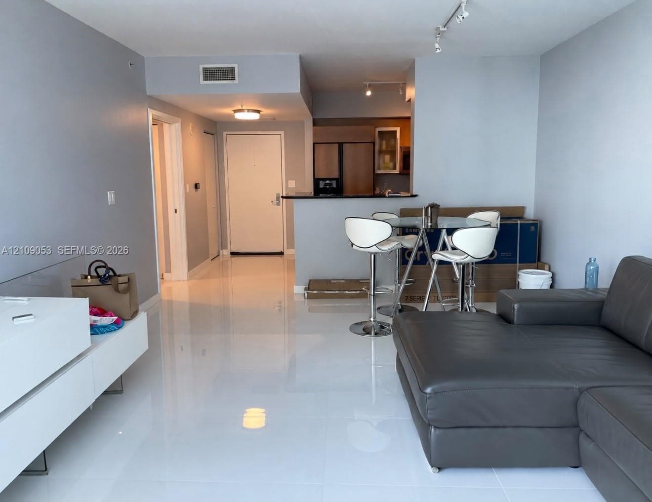 Open-concept floor plan with polished white tile flooring, track lighting, and a kitchen pass-through counter