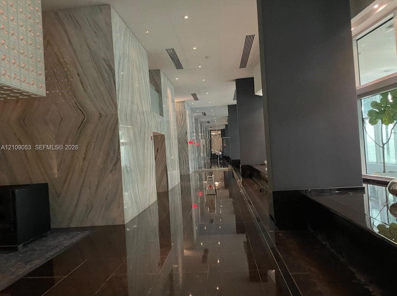 Expansive lobby featuring book-matched stone wall cladding, polished dark stone flooring, high-gloss structural columns, and recessed ceiling lighting