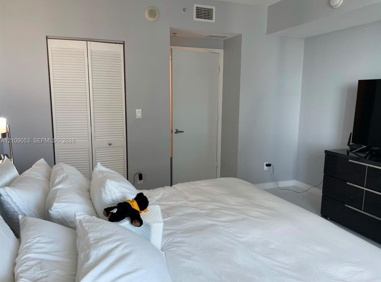 Room featuring neutral wall paint, white louvered-door closet, solid core interior door, and smooth-finish ceiling