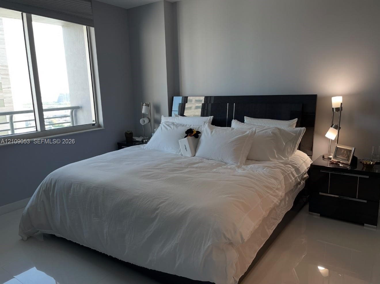 Bedroom featuring large-format polished tile flooring, expansive window, and integrated window shade